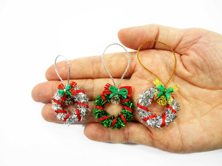 Comparison photo of three 1:12 scale miniature Christmas wreaths in green, silver, and silver with gold ribbon held in a palm for collectors.