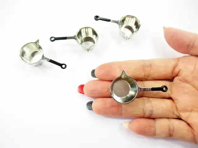 Adult hand showing the top-down view of a 1:12 scale silver metal saucepan for dollhouse cookware arrangements.