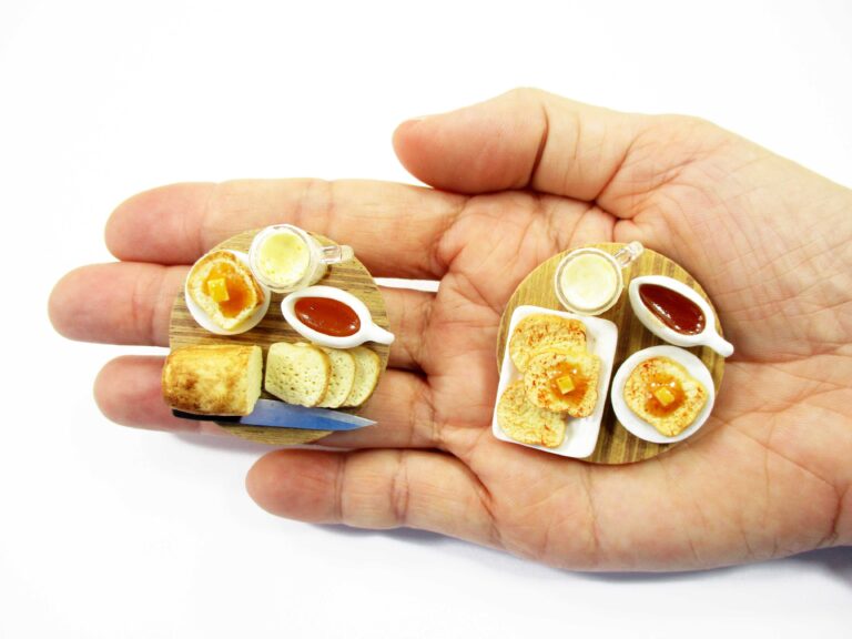 Hand holding 1:12 dollhouse miniature bread loaf set on wooden platter to show tiny handmade clay details.