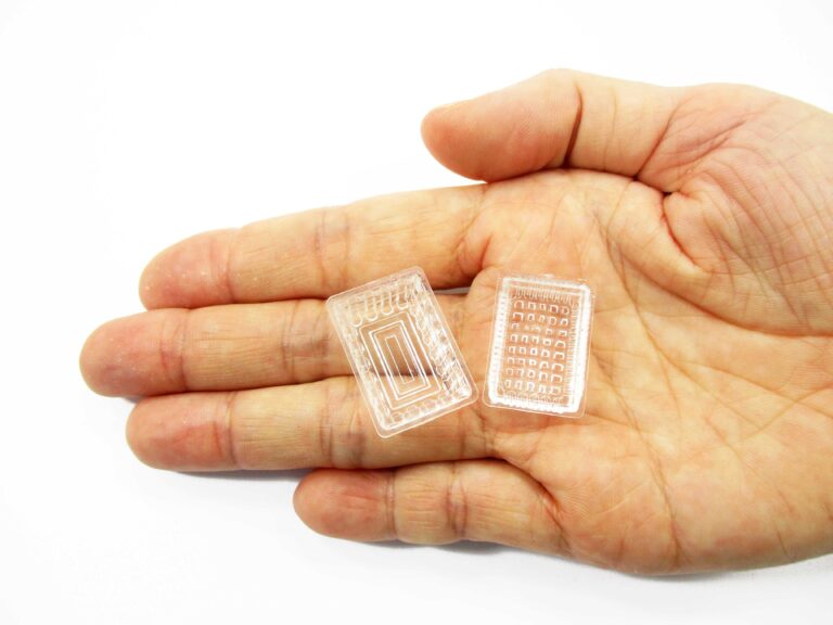 Hand holding 1:12 scale miniature clear acrylic food trays in both 17x25mm and 15x23mm sizes for dollhouses.