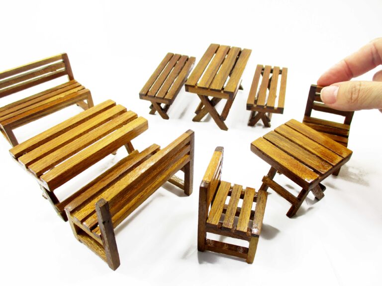 1:12 scale miniature wooden table with two slatted backrest chairs, warm varnished finish, shown front-on for scale and detail.