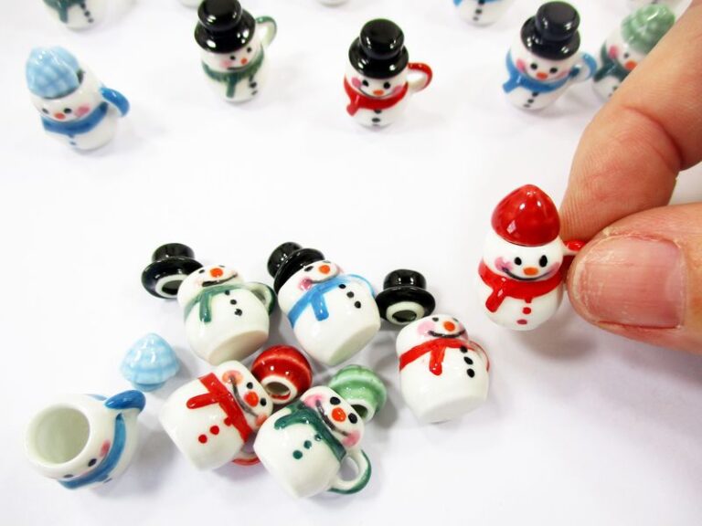 Held by fingertips a tiny 1:12 scale snowman ceramic mug with a red hat to show realistic size for dollhouse collectors.